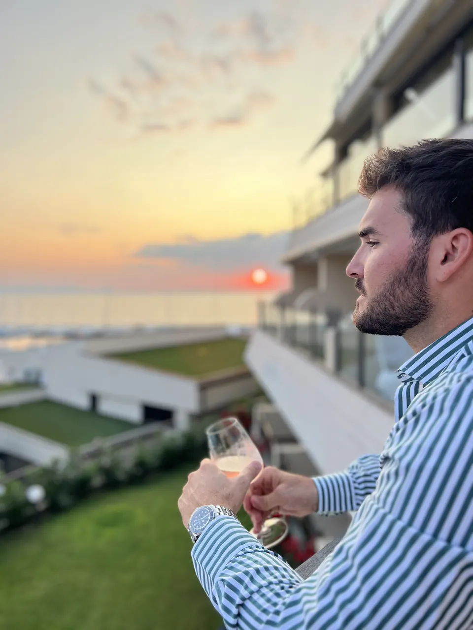 A man with a glass of wine on a terrace at sunset